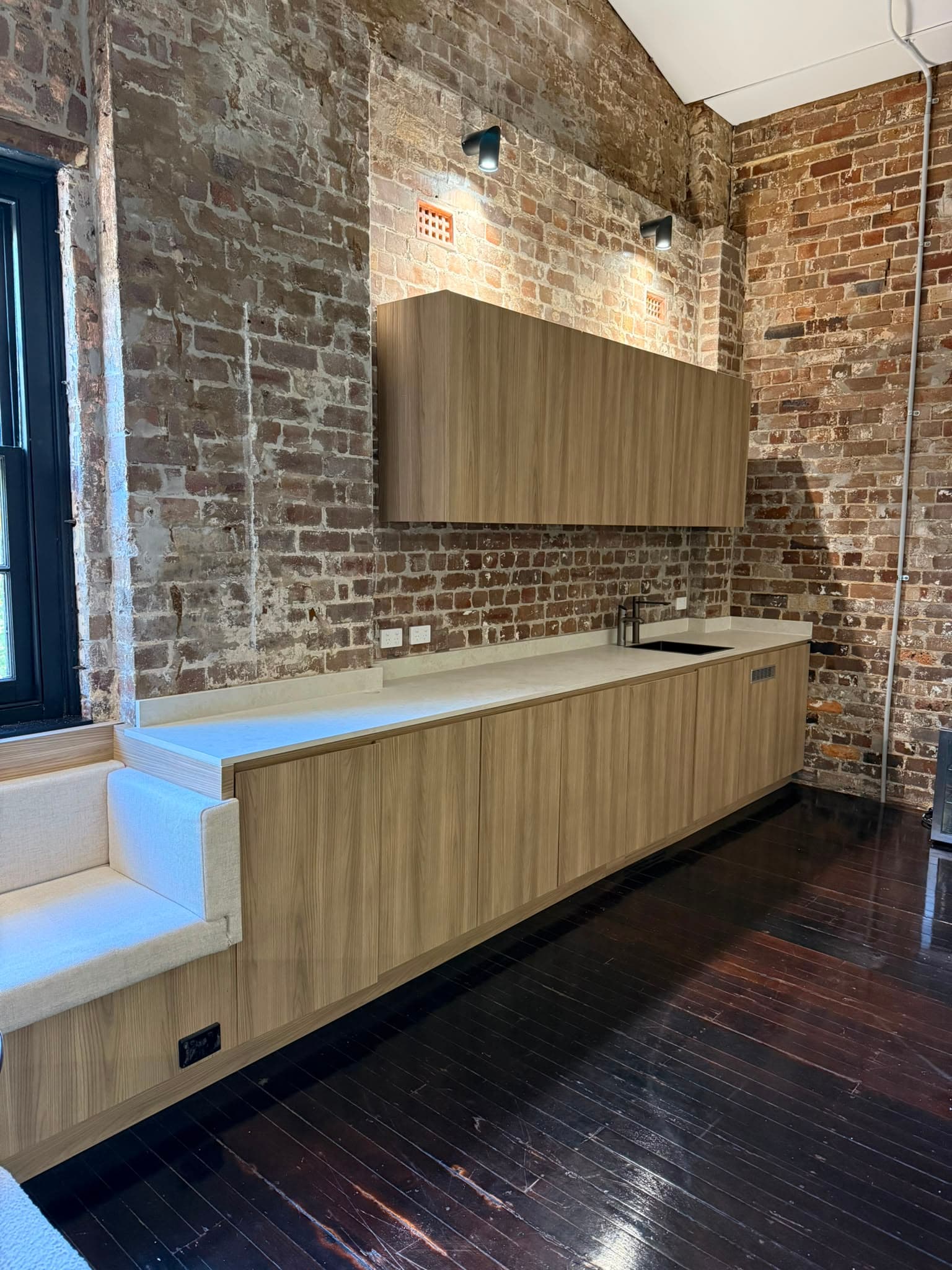 Timber kitchenette and built-in banquette against an exposed brick wall